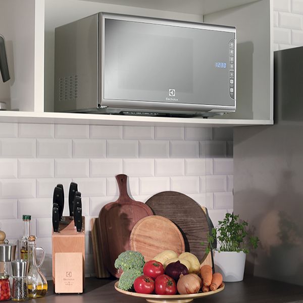Uma cozinha moderna com um elegante micro-ondas Electrolux MI41S sobre a bancada, cercado por eletrodomésticos de aço inoxidável e uma decoração limpa e minimalista.